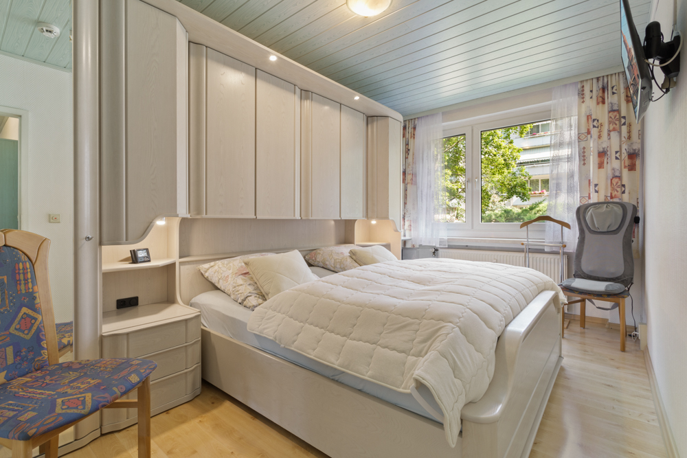 Helles Schlafzimmer mit Doppelbett, Einbauschränken und großem Fenster mit Vorhängen.