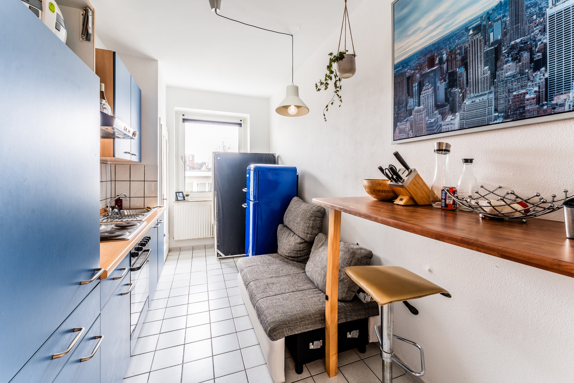 Schmale Küche mit blauen Schränken, kleinem Sofa, Holztresen und großem Fenster.