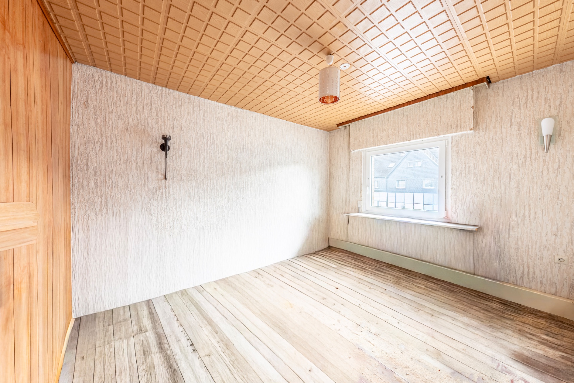 Leerer Raum mit Holzboden, heller Tapete, Fenster und Holzdecke.