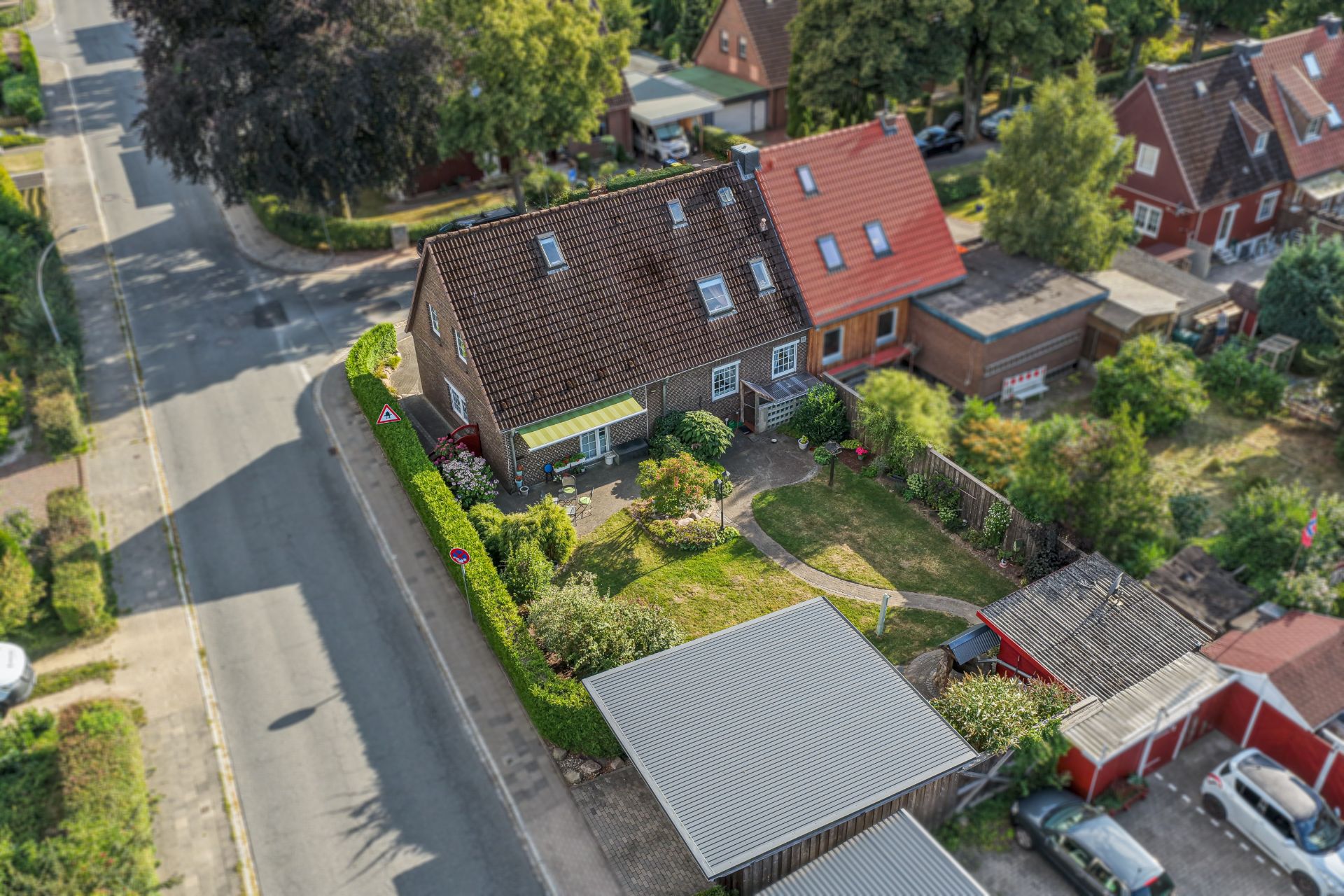Luftbild eines Einfamilienhauses mit Garten, Carport und angrenzender Straße.