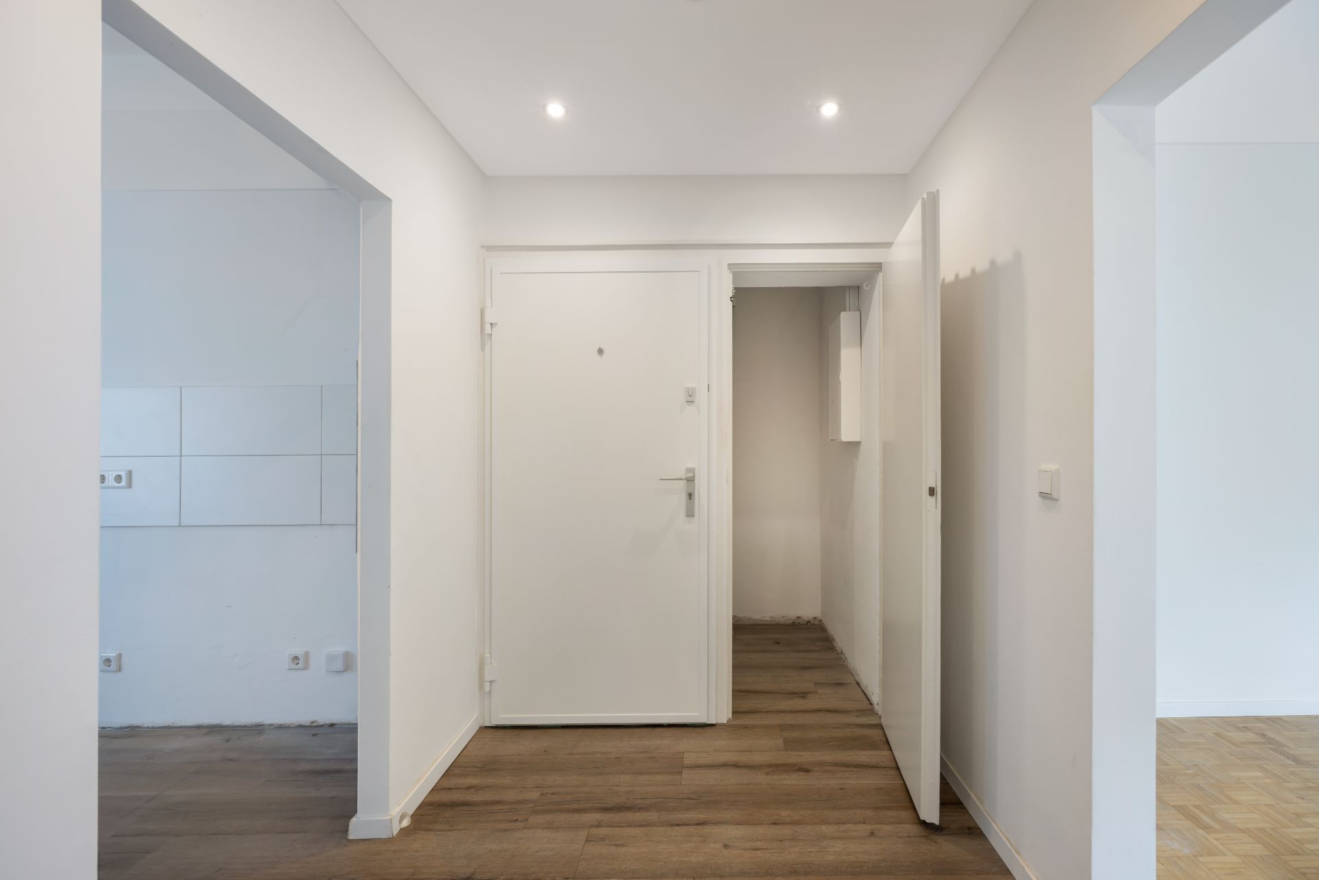 Heller Flur mit Holzboden, mehreren Türen und weißen Wänden.