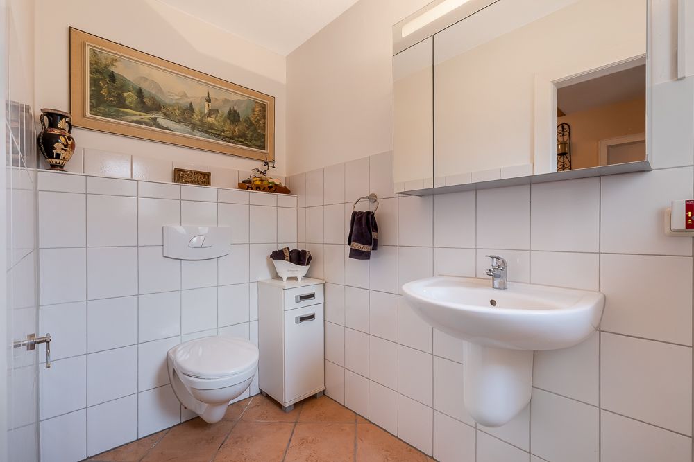 Badezimmer mit Wandtoilette, Waschbecken, Spiegelschrank und Dekoration an den Wänden.