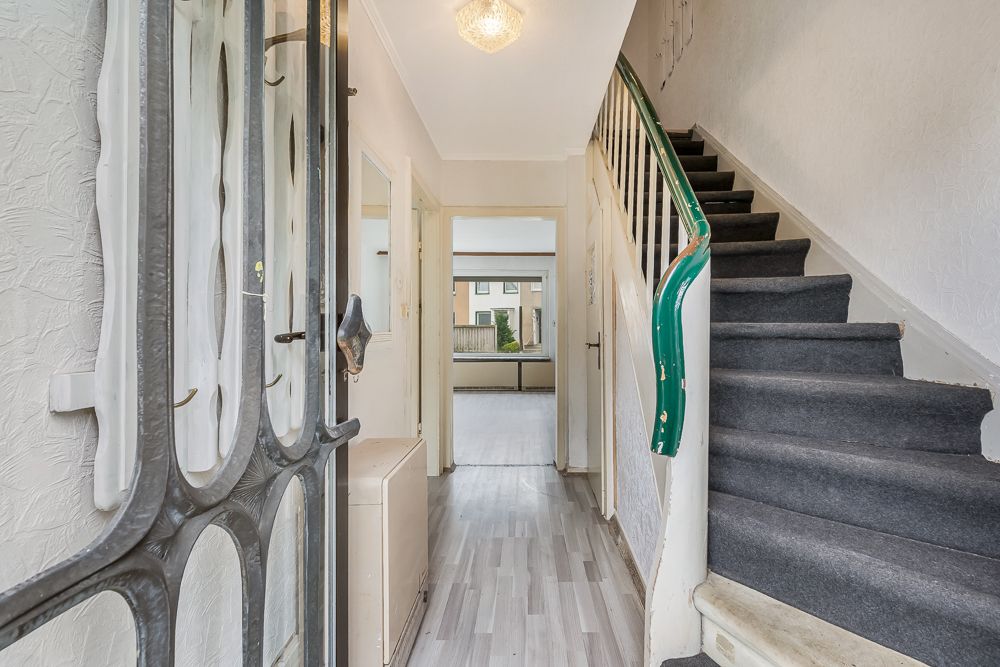 Eingangsflur mit Treppe und Blick in ein helles Zimmer. Teppich auf der Treppe, Laminatboden im Flur.