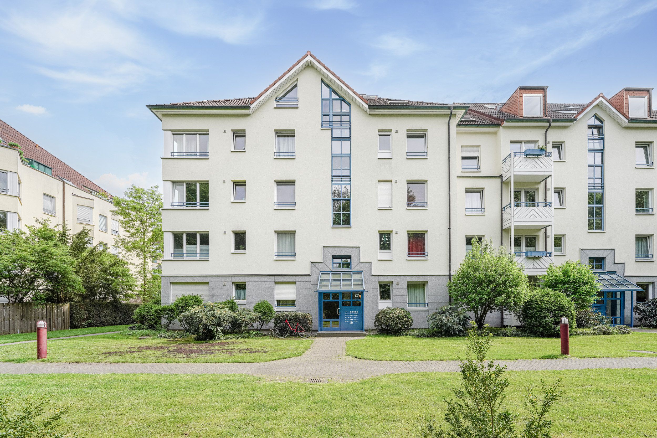 Mehrfamilienhaus mit mehreren Balkonen und einem gepflegten Garten im Vordergrund.