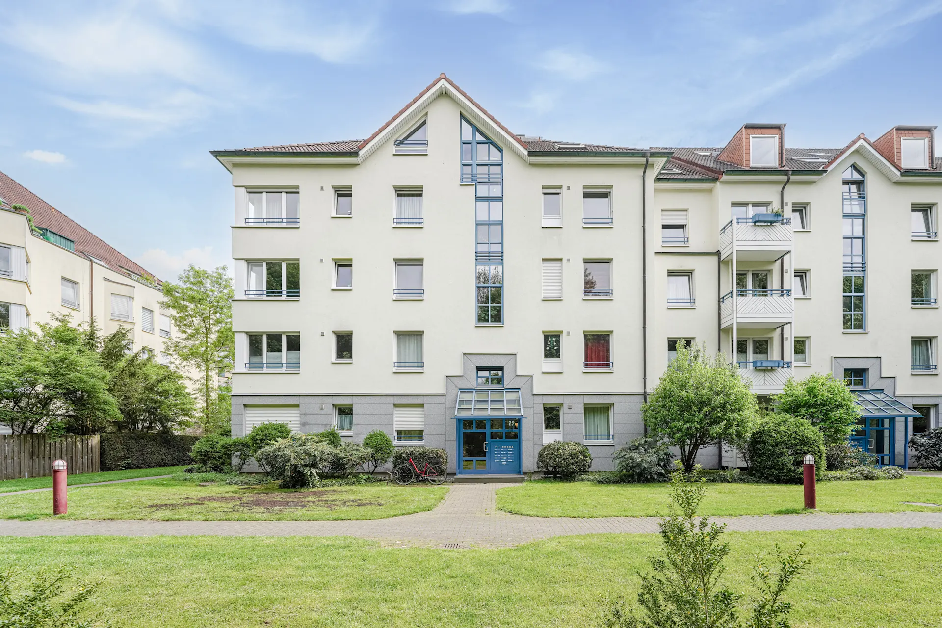 Mehrfamilienhaus mit mehreren Balkonen und einem gepflegten Garten im Vordergrund.