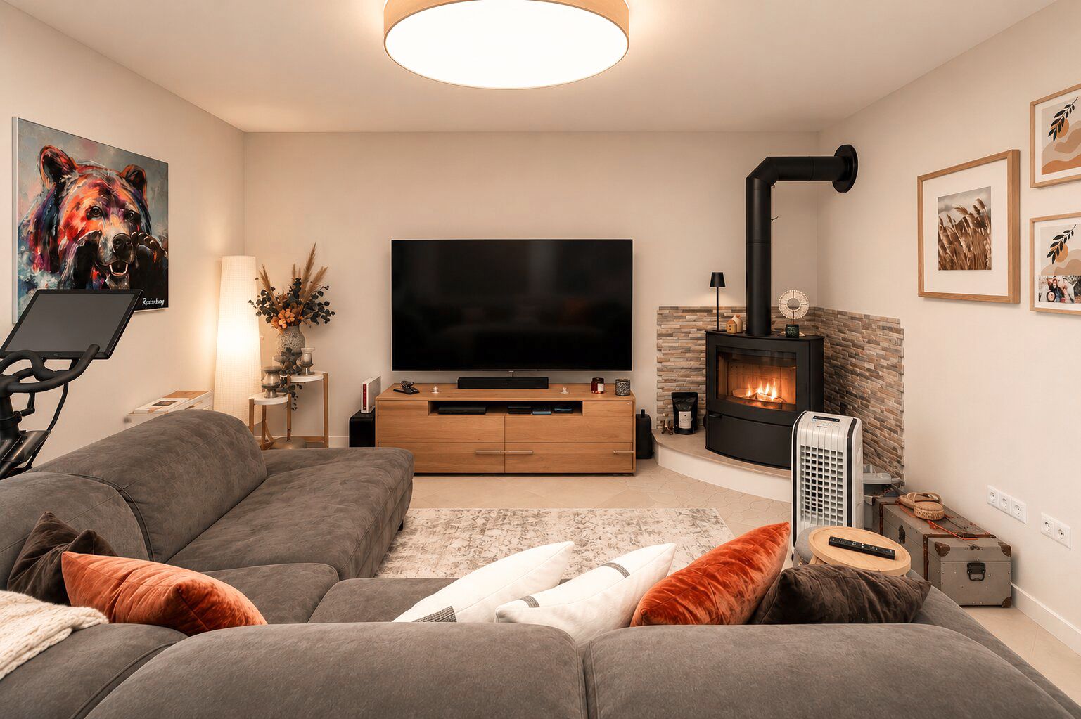 Modernes Wohnzimmer mit grauem Sofa, großem Fernseher und Kaminofen.