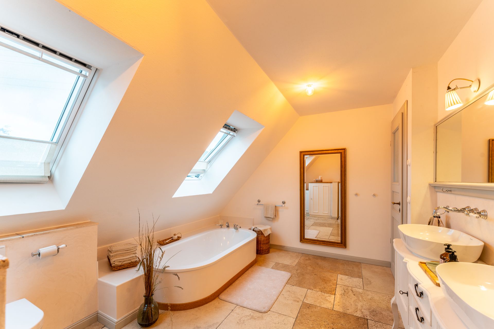 Helles Badezimmer mit Badewanne, zwei Dachfenstern, großem Spiegel und Doppelwaschbecken.