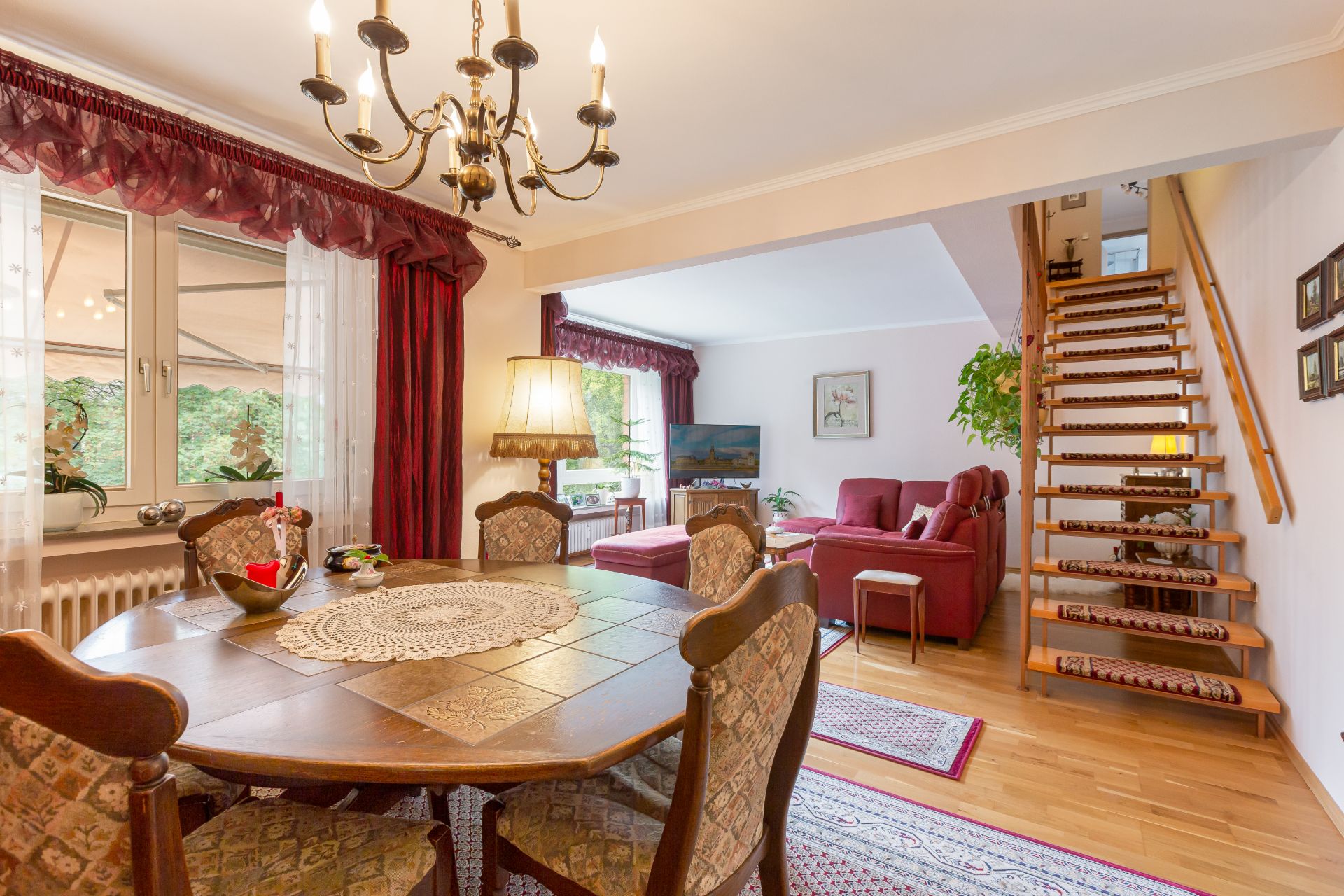 Esszimmer mit rundem Tisch, Kronleuchter, Sofa-Ecke und Holztreppe in einem Wohnhaus.