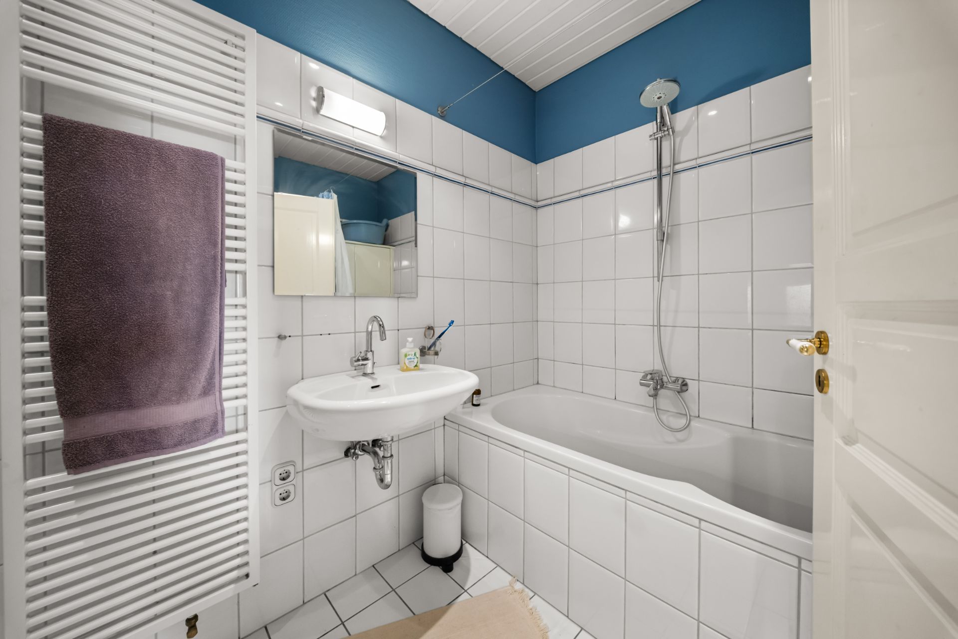 Helles Badezimmer mit Badewanne, Waschbecken, Spiegel und Handtuchheizkörper.
