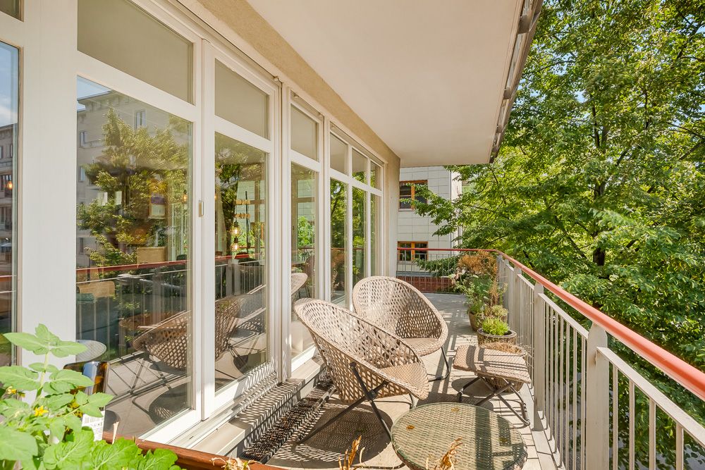 Balkon mit Rattanmöbeln, Pflanzen und Blick auf Bäume und Nachbargebäude.