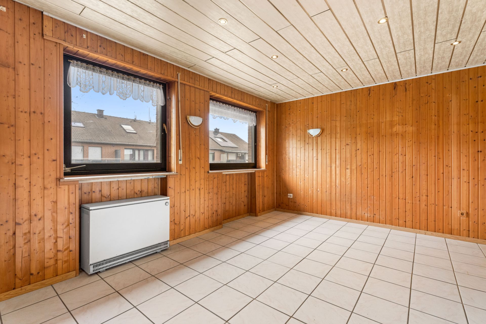 Leerer Raum mit Holzverkleidung, zwei Fenstern und weißem Fliesenboden.