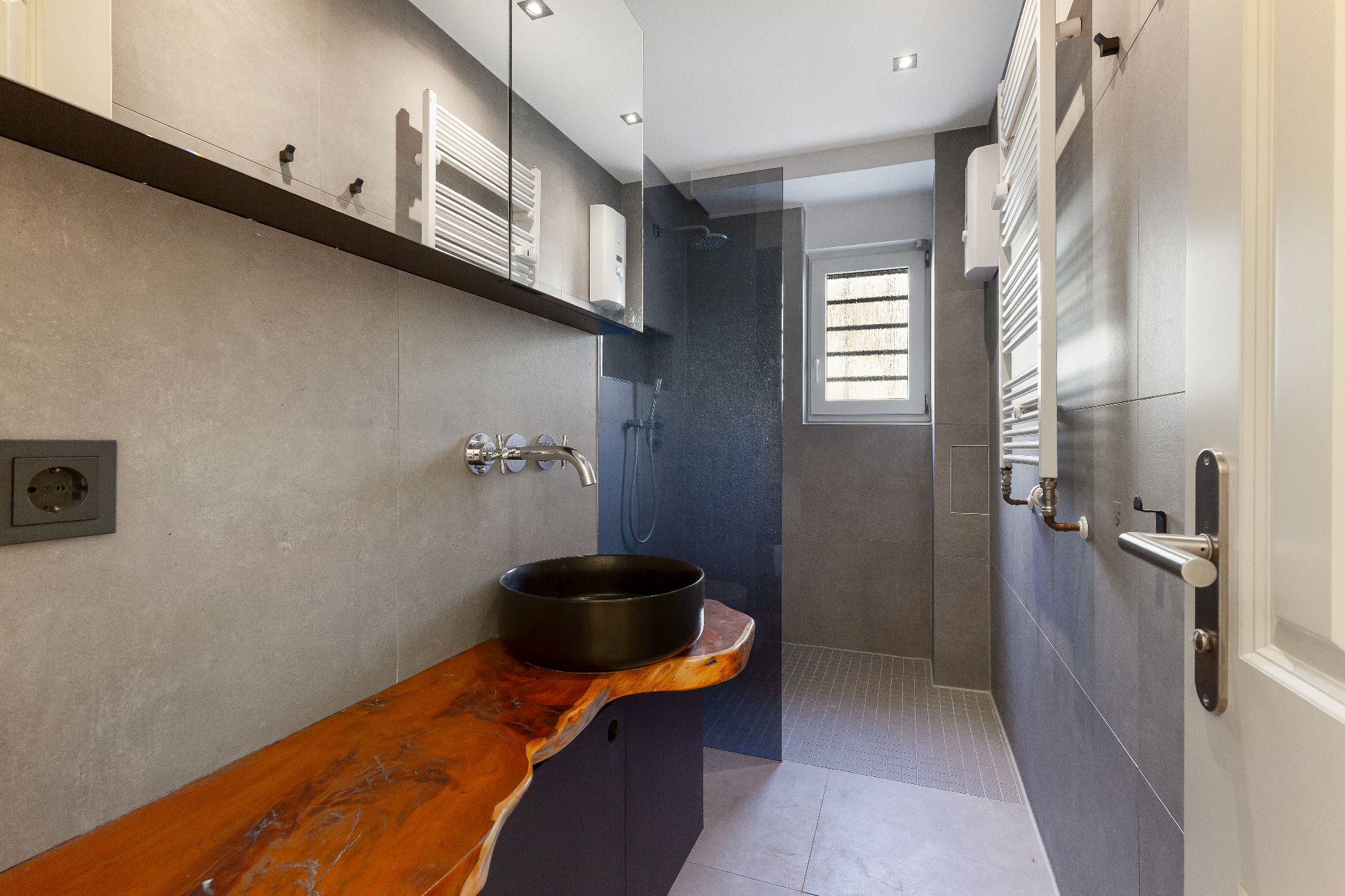 Modernes Bad mit Holzwaschtisch, schwarzem Waschbecken und bodengleicher Dusche.