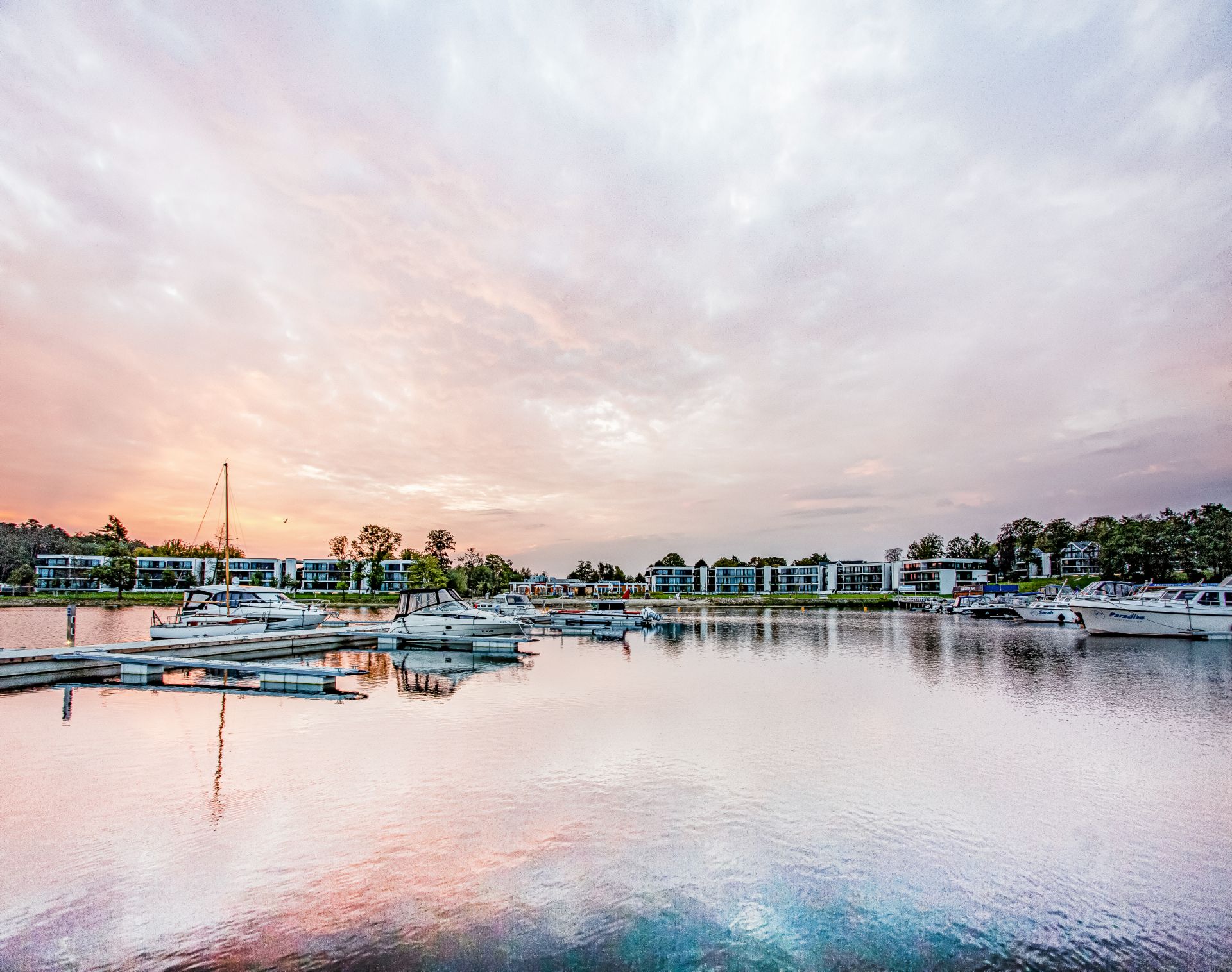 Boote liegen an einem modernen Yachthafen vor Wohngebäuden bei Sonnenuntergang.