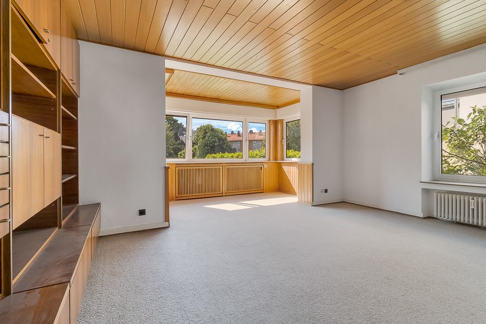 Helles Wohnzimmer mit großen Fenstern, Holzboden an der Decke und Einbauschrank links.