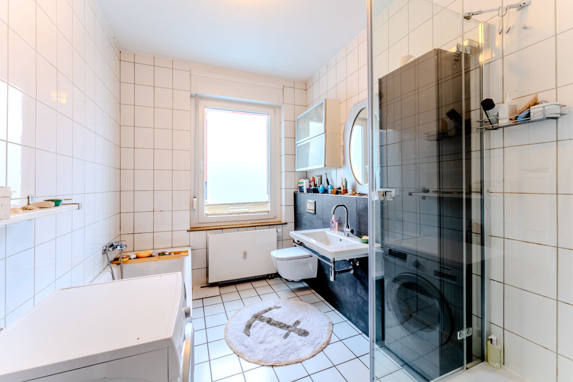 Helles Badezimmer mit Dusche, Badewanne, Waschbecken, Toilette, Waschmaschine und Fenster.