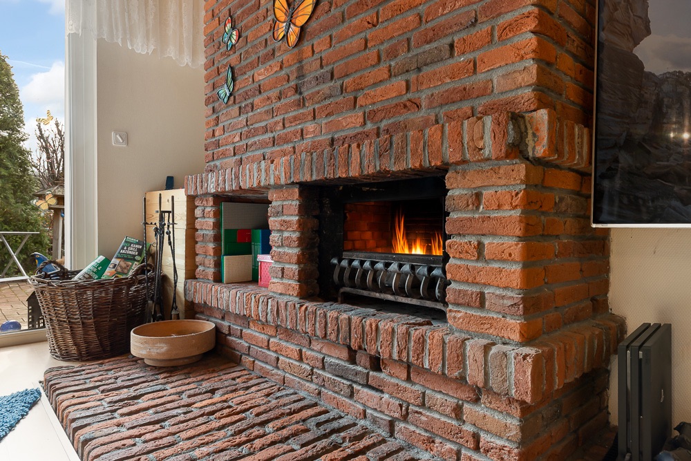 Kamin aus roten Backsteinen mit Feuer, Dekoschmetterlingen und Korb auf der Seite.