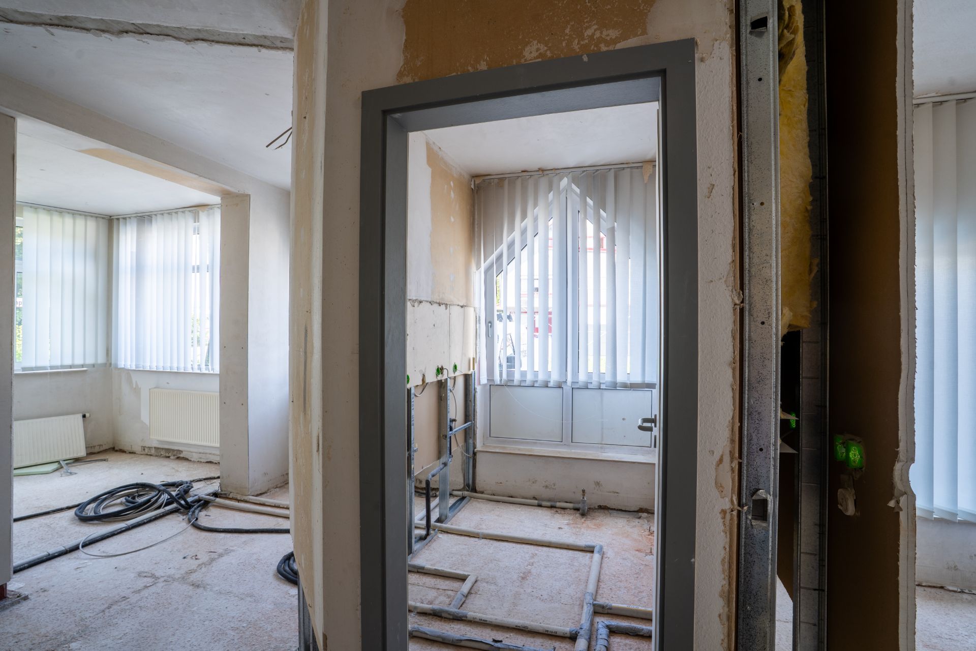 Renovierungsarbeiten in einem hellen Raum mit großen Fenstern und sichtbaren Heizkörpern.