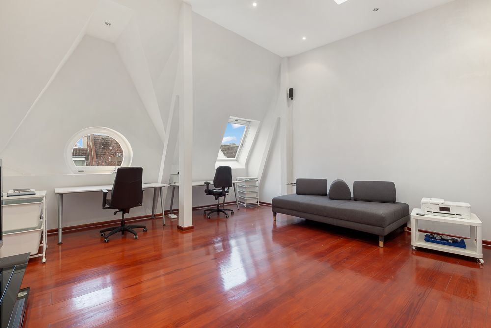 Heller Raum mit Holzfußboden, zwei Schreibtischen, zwei Stühlen und einem grauen Sofa.