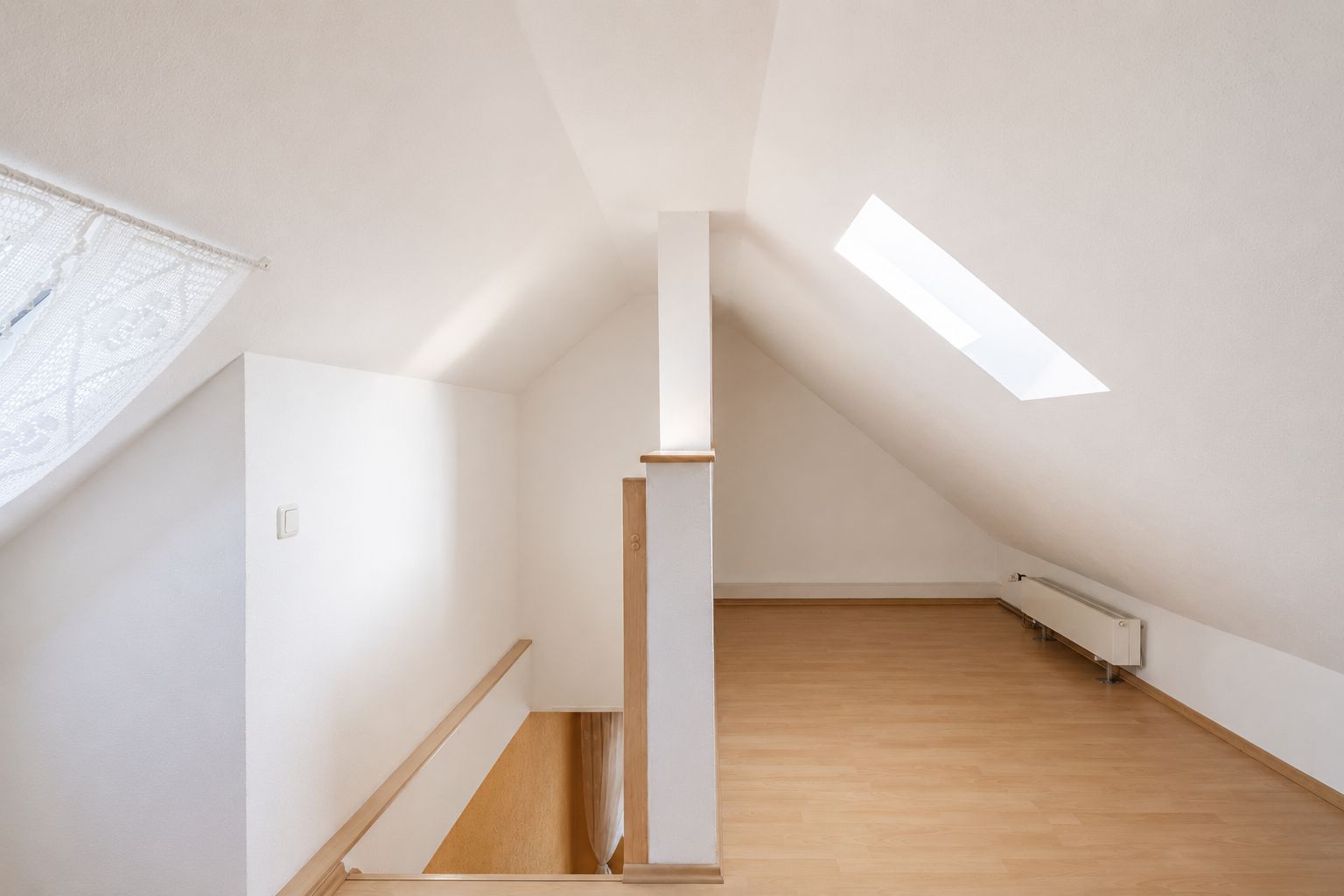 Heller Dachbodenraum mit Holzfußboden, Dachfenster und sichtbarer Treppe.