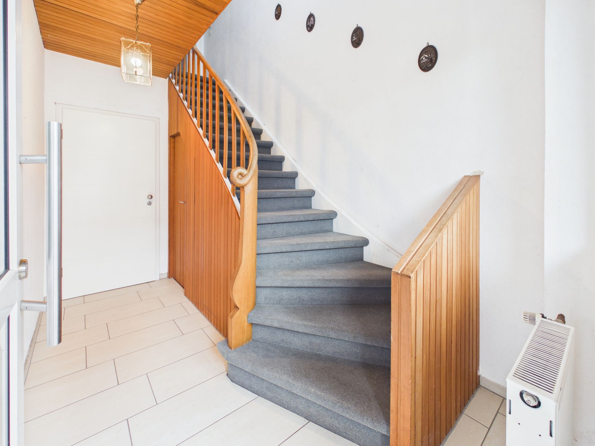 Flur mit Teppichtreppe, Holzgeländer und weißen Wänden, daneben Heizung und Wanddekoration.