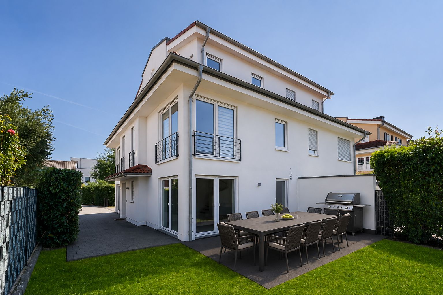 Moderne weiße Wohnhaus mit Garten, Terrasse, Esstisch und Grill im Außenbereich.