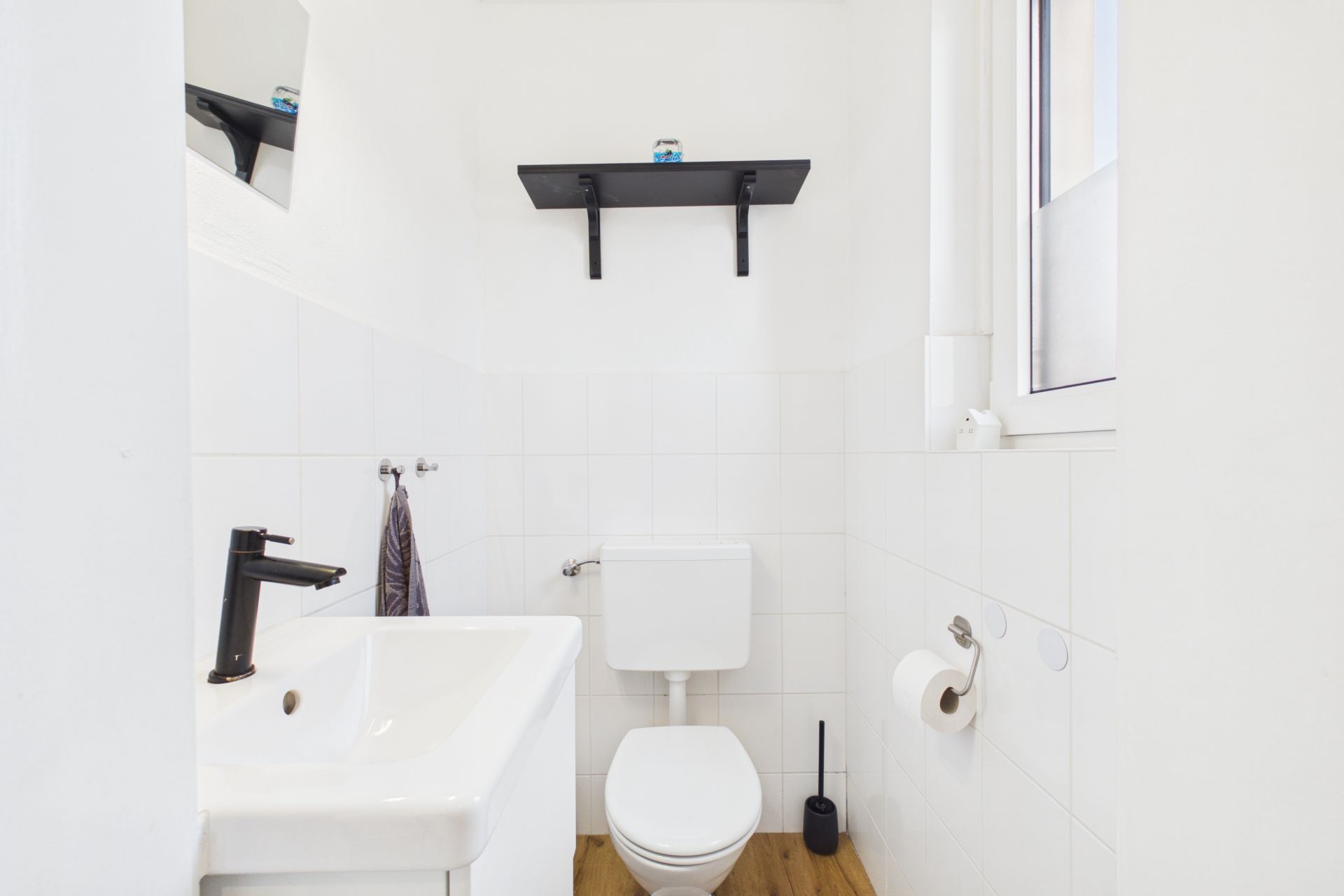 Kleines, helles Bad mit WC, Waschbecken, Spiegel und Fenster.