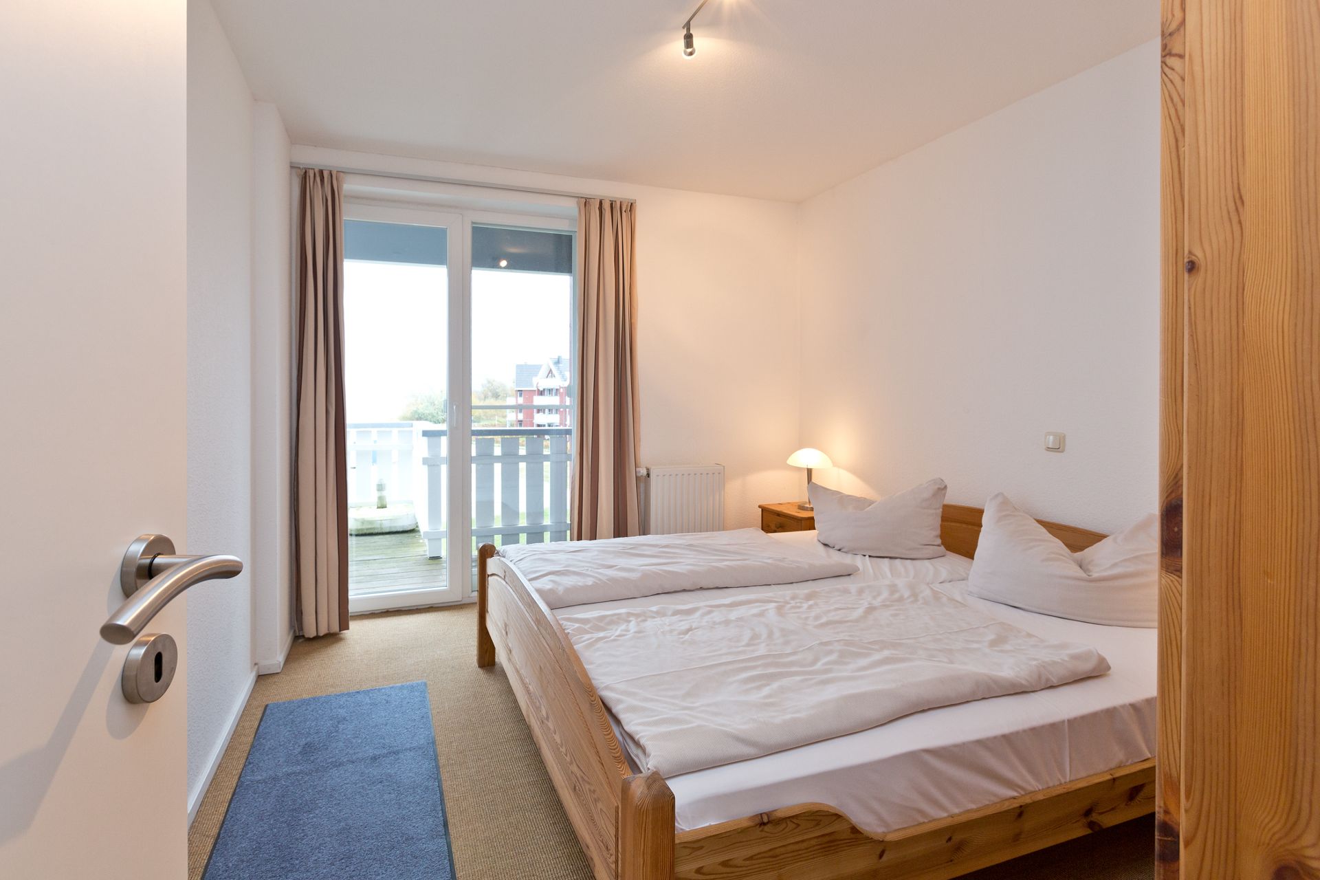 Helles Schlafzimmer mit Doppelbett, Nachttisch, Lampe und Zugang zu einem Balkon.