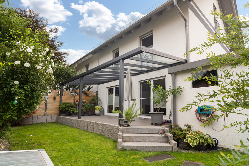 Moderne Terrasse mit Glasdach und Pflanzen im Garten eines Wohnhauses.