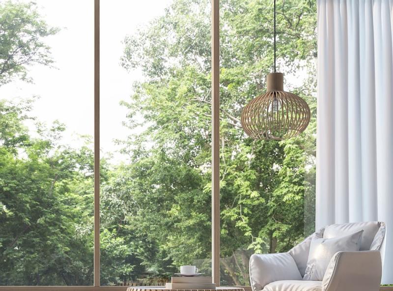 Heller Raum mit Sessel, rundem Holztisch und großem Fenster mit Blick ins Grüne.