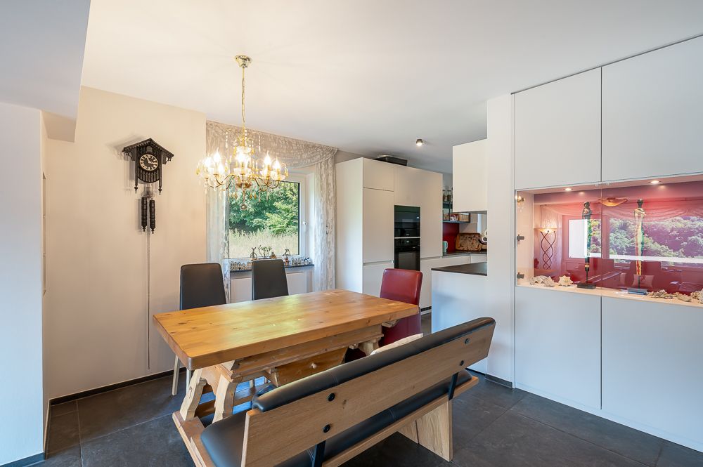 Essbereich mit Holztisch, Bank, Stühlen, Kronleuchter und Kuckucksuhr an der Wand.