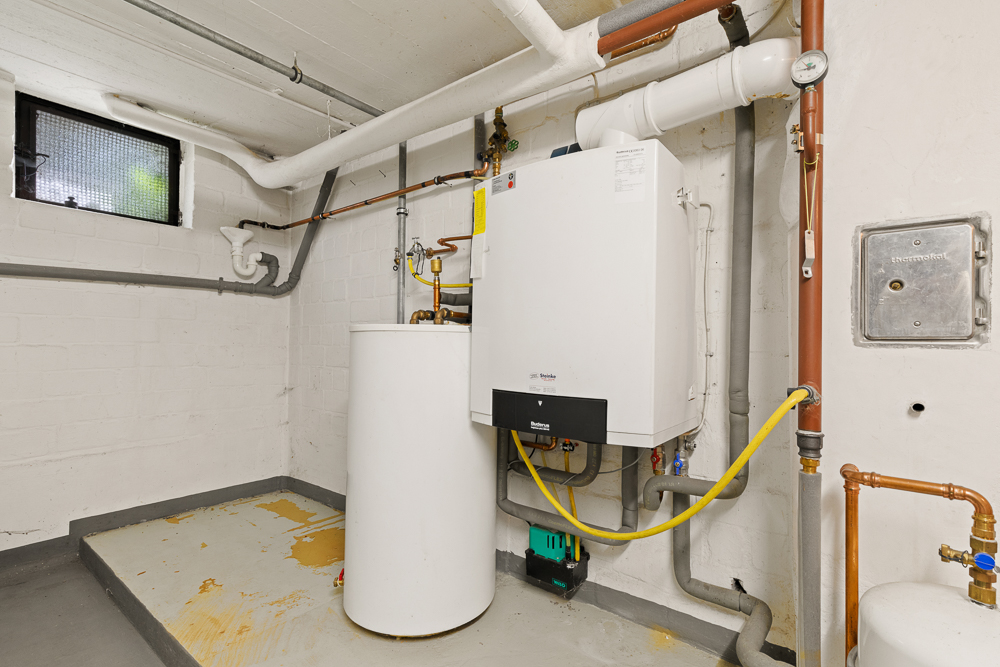 Heizungskeller mit Wandheizung, Rohren und Boiler, Fenster oben links an der Wand.