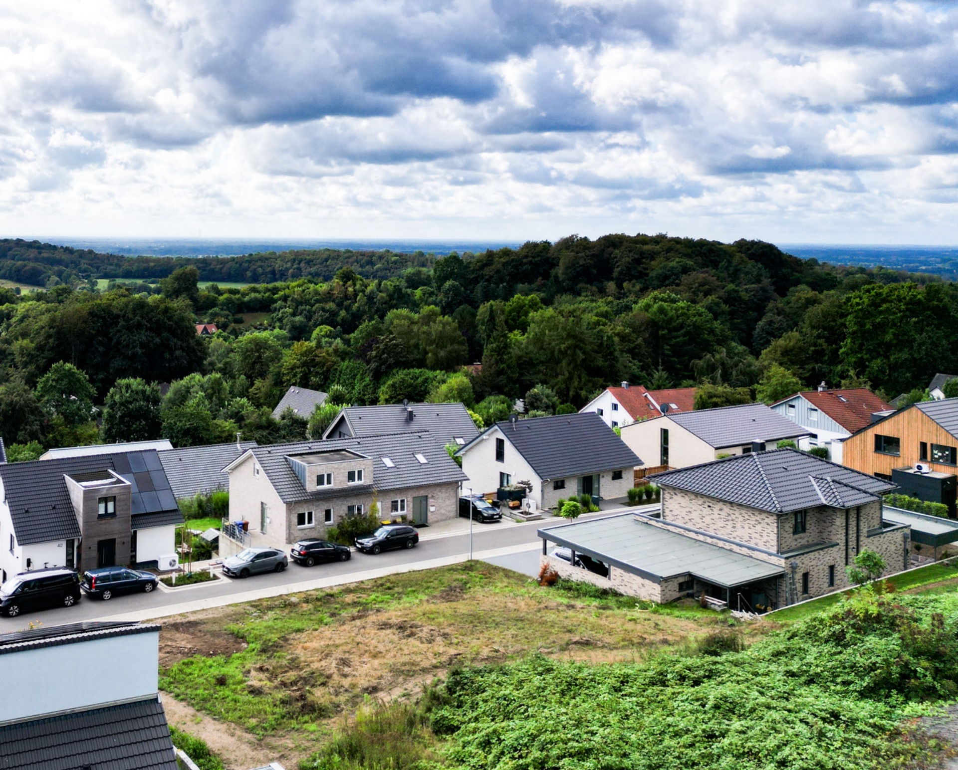 Mehrere Einfamilienhäuser an einer ruhigen Straße, umgeben von viel Grün und Bäumen.