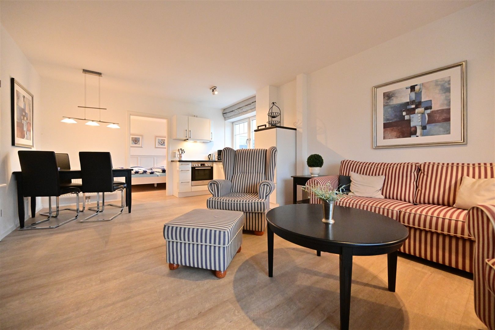 Wohnzimmer mit gestreiftem Sofa, Sessel, Esstisch, Küche im Hintergrund und moderner Dekoration.