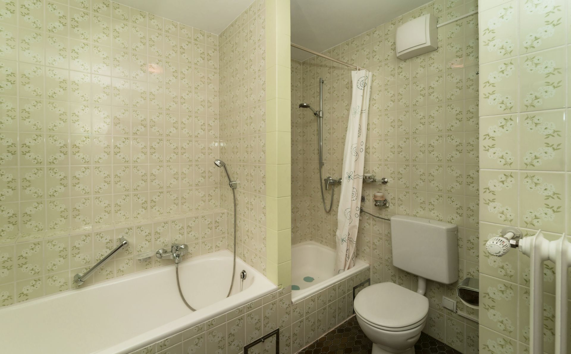 Badezimmer mit Badewanne, Dusche, Toilette und gemusterten Fliesen.