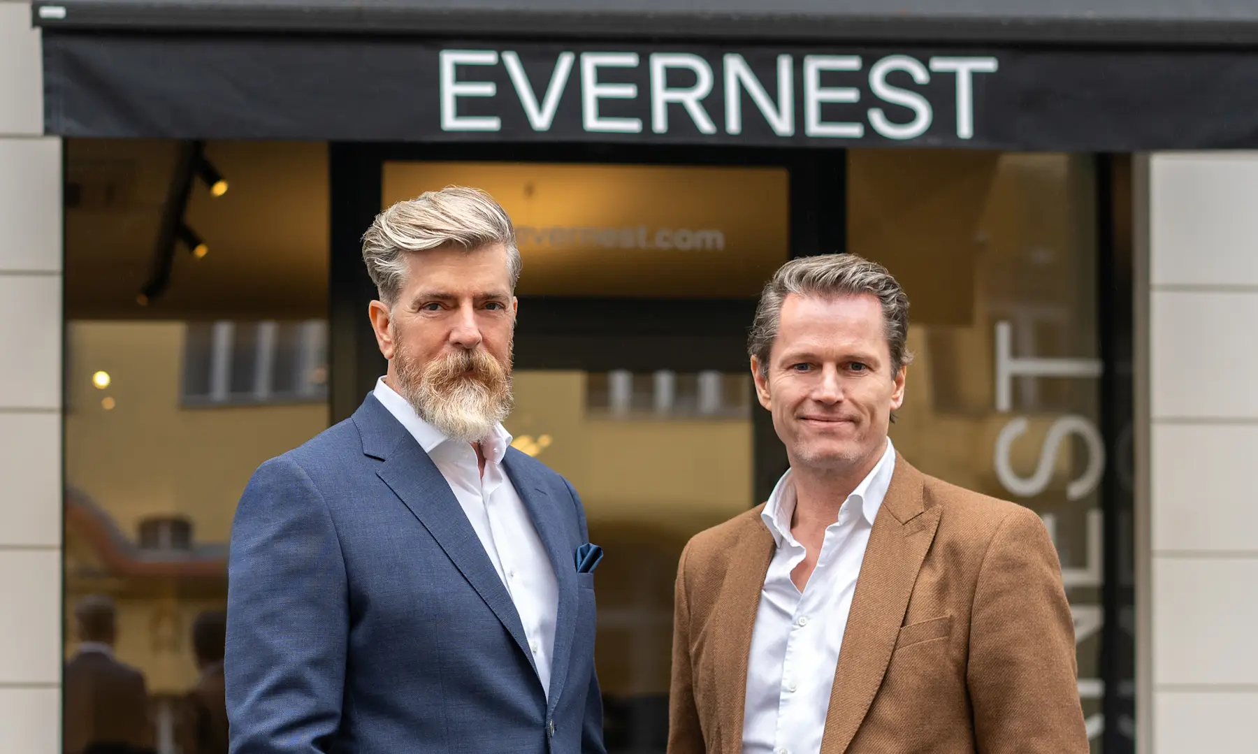 Zwei Männer in Anzügen stehen vor einem Geschäft mit dem Schild EVERNEST.