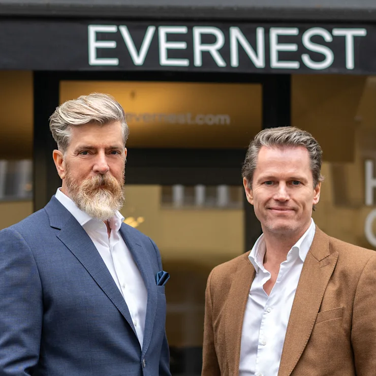 Zwei Männer in Anzügen stehen vor einem Geschäft mit dem Schild EVERNEST.