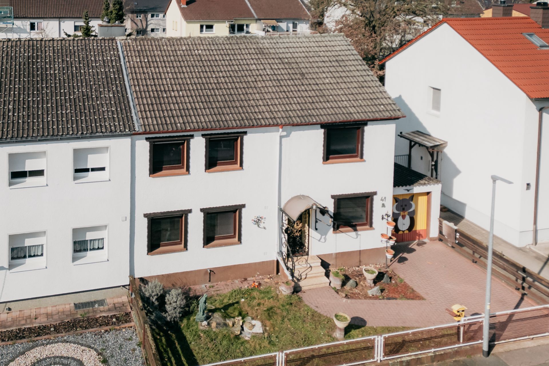 Zweistöckiges weißes Wohnhaus mit Garten, braunen Fensterrahmen und überdachtem Eingang.