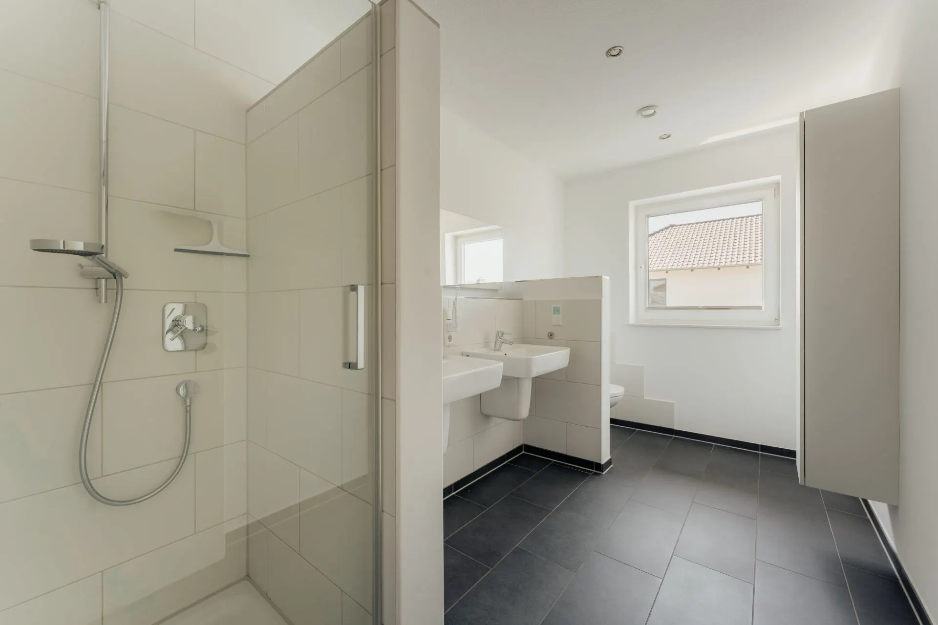 Modernes Badezimmer mit Dusche, zwei Waschbecken, Toilette und Fenster.