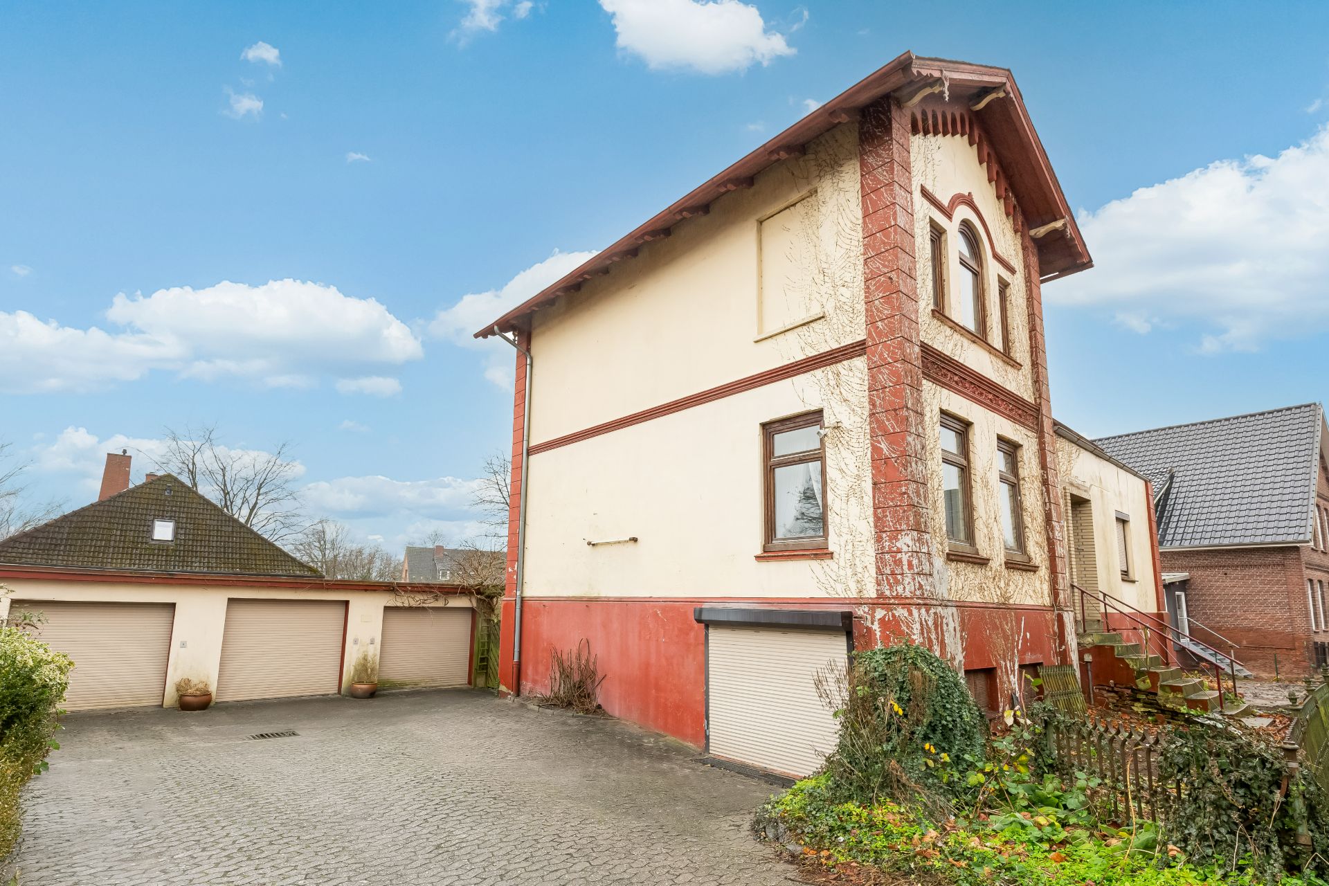 Zweistöckiges Wohnhaus mit roten Details, davor Garagen und Einfahrt, seitlich Treppe.