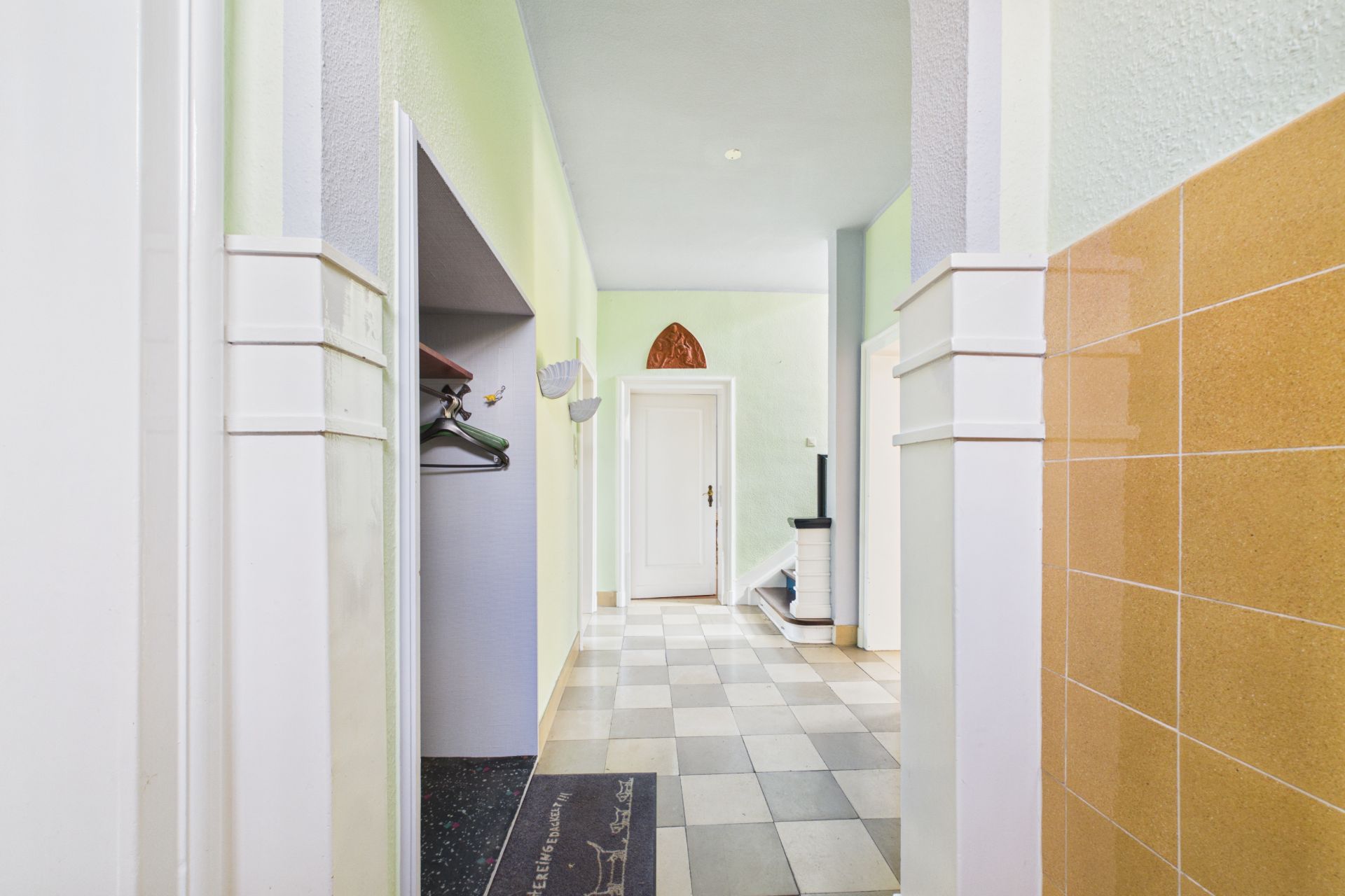 Heller Flur mit kariertem Boden, Garderobe und weißer Tür am Ende.