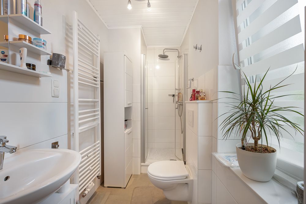 Modernes Badezimmer mit Dusche, Waschbecken, Toilette und einer Pflanze am Fenster.