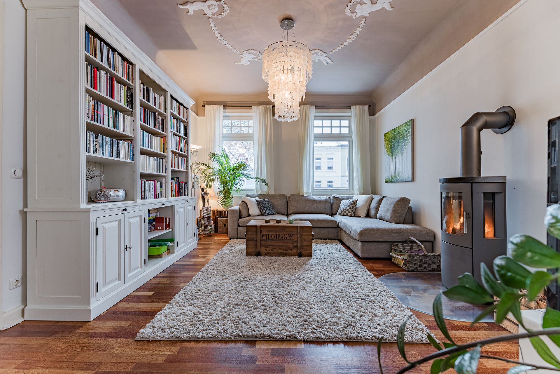Helles Wohnzimmer mit Bücherregal, Ecksofa, Kamin, Kronleuchter und Teppich.