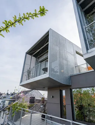 Moderne Wohnhausfassade mit Balkonen und Pflanzen im Vordergrund.