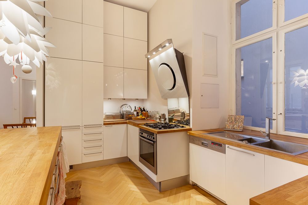 Moderne Küche mit Holzarbeitsflächen, weißen Schränken, Herd, Spüle und großem Fenster.