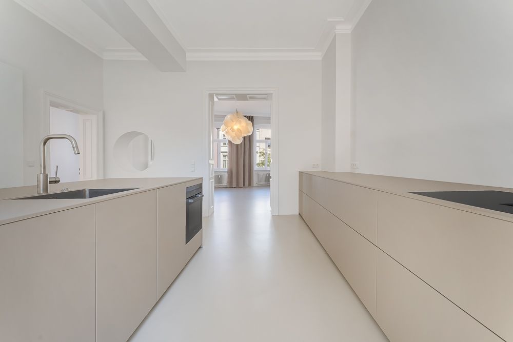 Helle, moderne Küche mit beigen Schränken, Spüle und Herd, Blick in einen weiteren Raum.