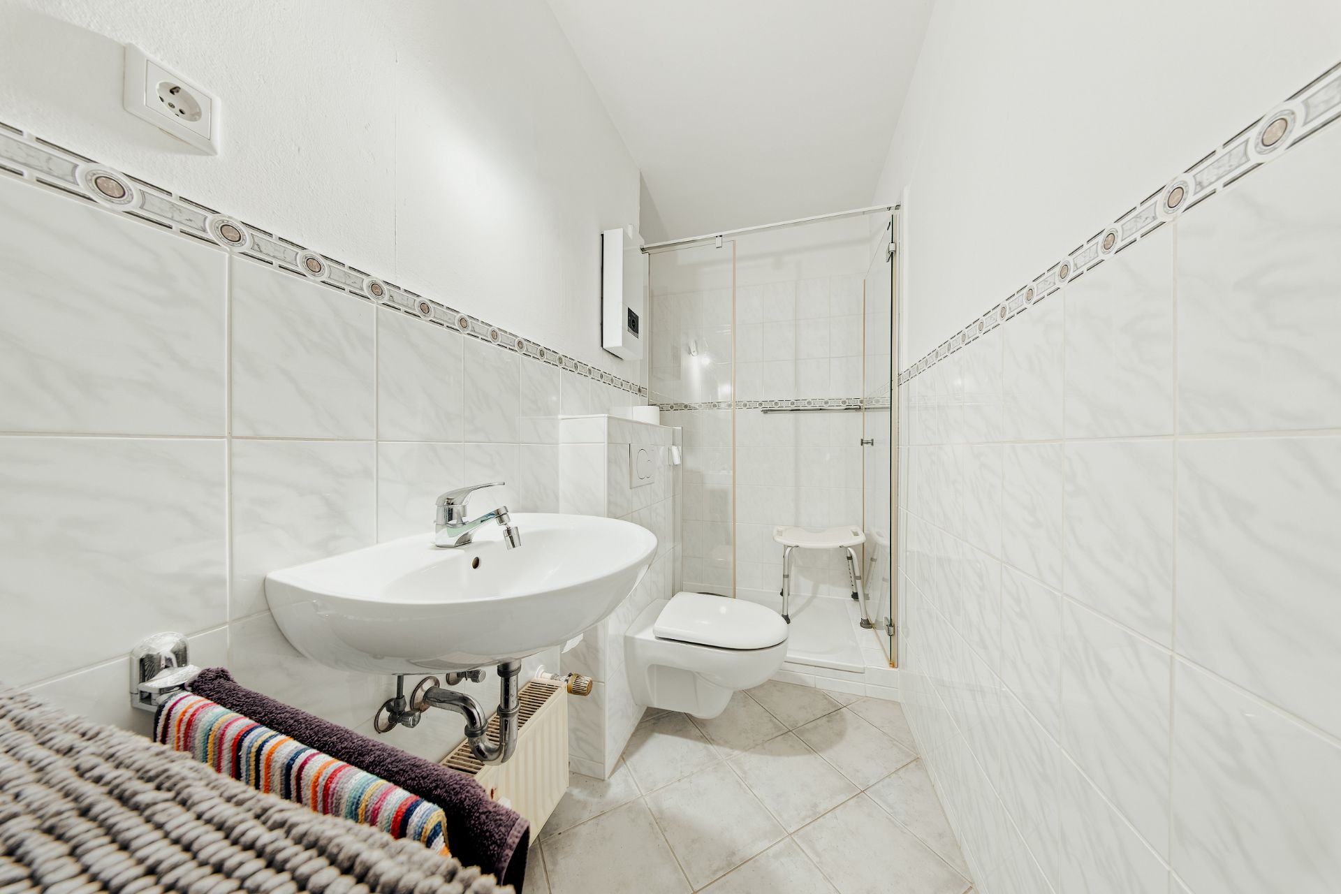 Helles Badezimmer mit Waschbecken, WC, Dusche und Handtüchern auf einem Regal.