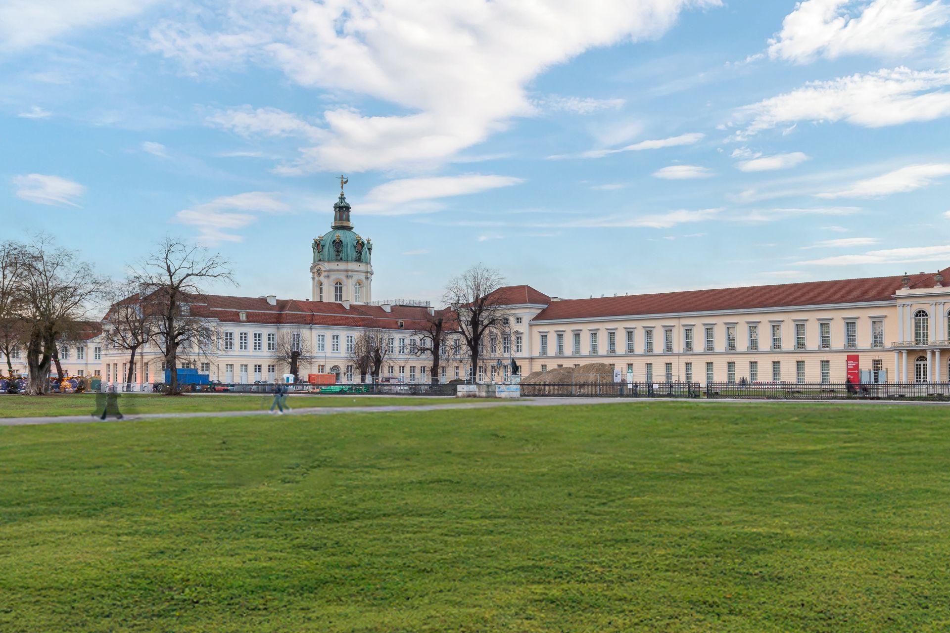 Großes historisches Gebäude mit rotem Dach, Turm und davor eine große Rasenfläche.