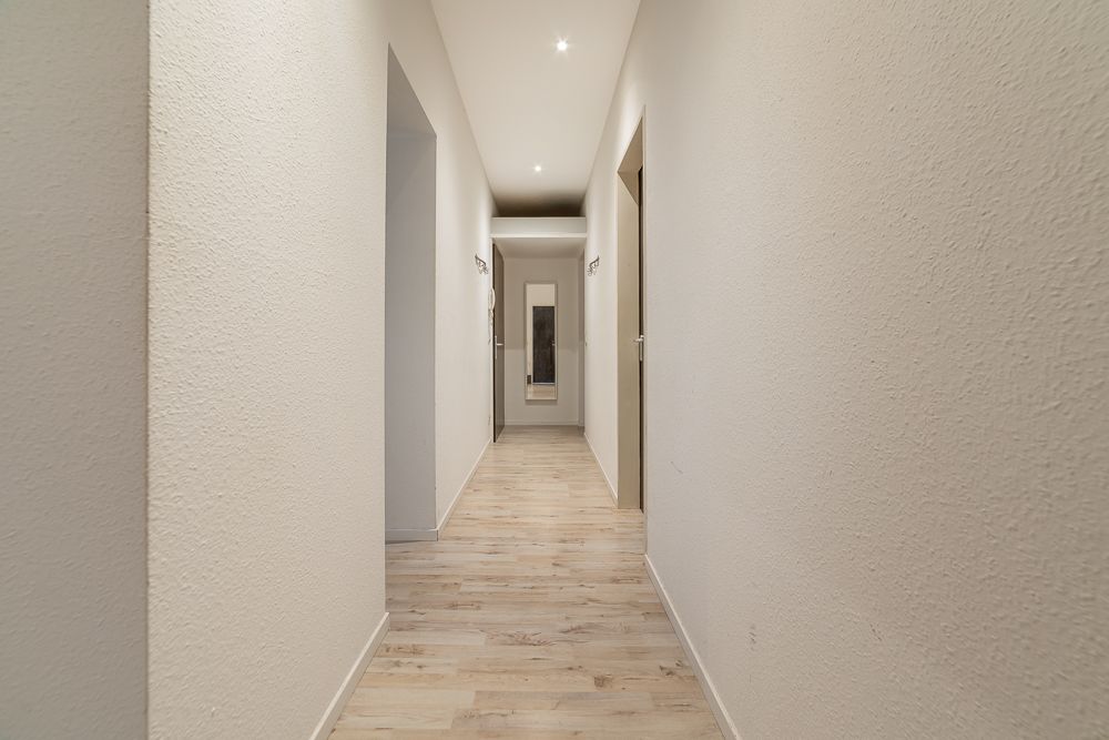 Heller Flur mit Holzboden und mehreren Türen, am Ende ein Spiegel an der Wand.