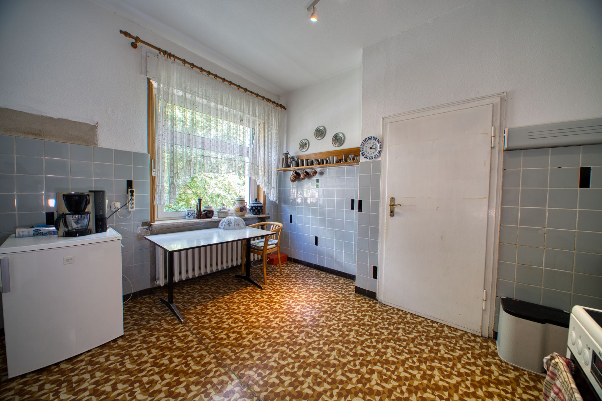Küche mit kleinem Kühlschrank, Esstisch, Stühlen und Geschirrregal an der Wand.
