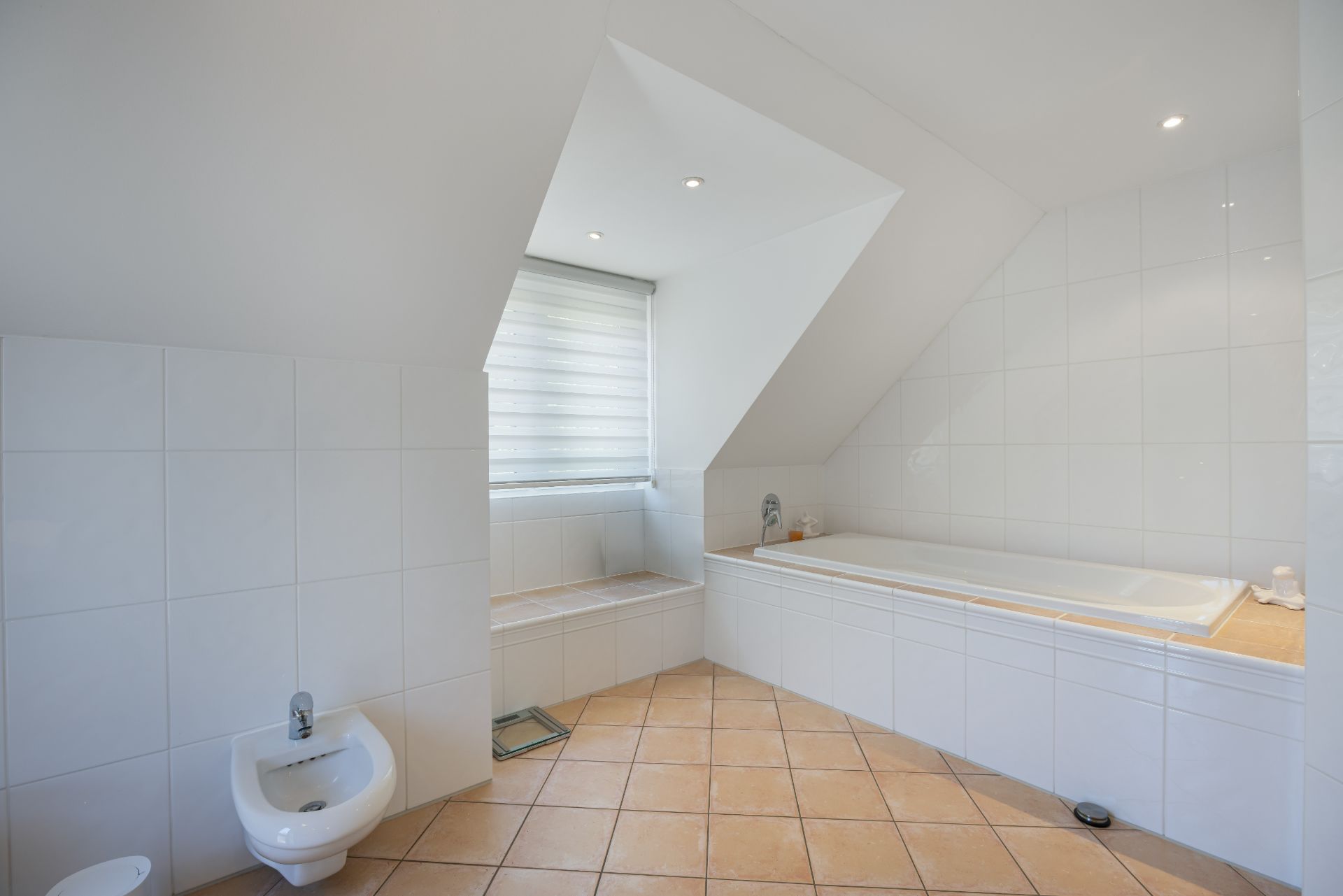 Modernes Badezimmer mit Badewanne, Bidet und Fenster unter einer Dachschräge.